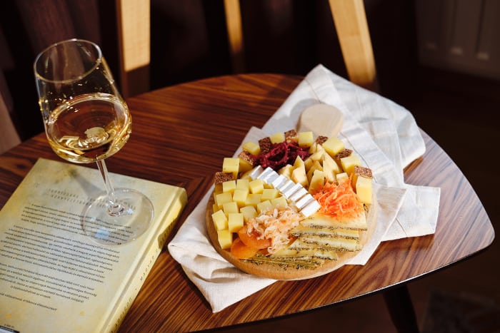 fermentált savanyúságok sajtos étel mellé tálalva egy pohár bor mellett