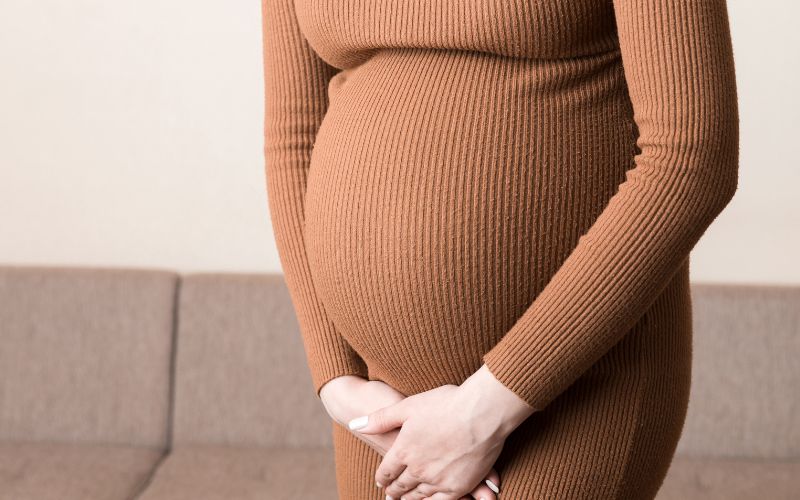 inkontinenciával küzdő várandós nő a húgyhólyag irányába mutató kezekkel