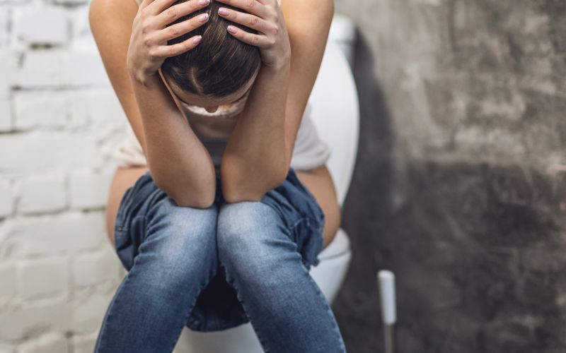 vizelettartási problémával küzdő nő ül a wc-n fejét szomorúan előre hajtva